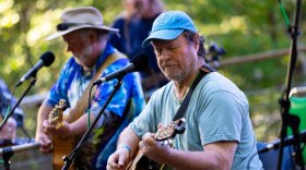 Men play guitar on an outdoor stage.
