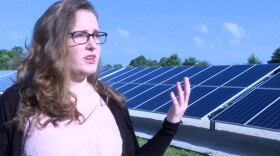 Indiana University student Savannah Rodrigue stands in front of a solar array next to a water booster station in Bloomington which helps to offset some of the station's energy use.