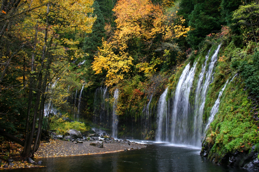 Water cascades over a moss-covered cliff at Mossbrae Falls near Dunsmuir, California, forming multiple thin streams into a shallow pool below.