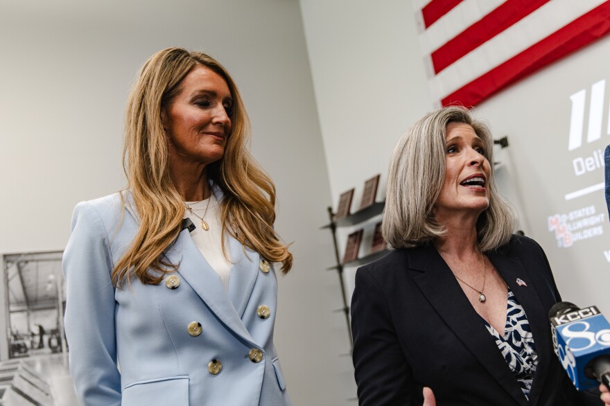 Two women stand in an office building with an American flag.