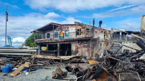 People stand on the roof of a fire-damaged building in Puerto Rico. A pile of burned rubble is in the right foreground.