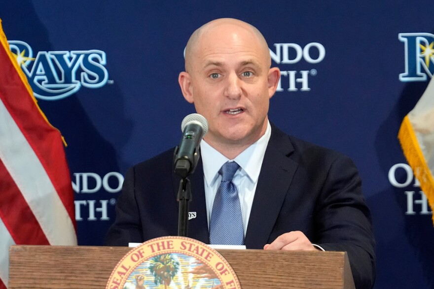 Bald man in a dark suit speaking behind a podium