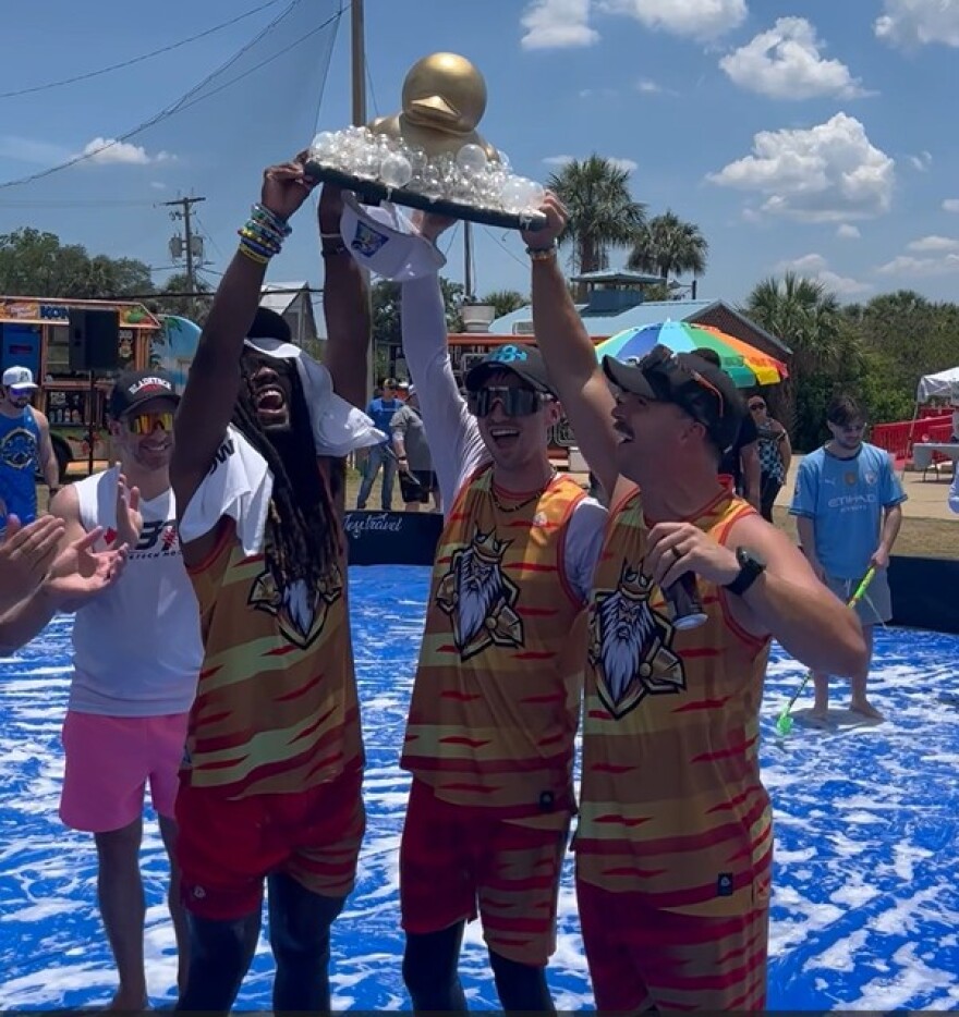 Three men hold a golden duck soap trophy 