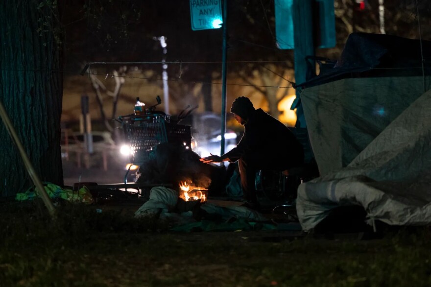 Muhammad, who declined to provide his last name, warms his hand at a fire near his tent in Sacramento on Feb. 24, 2022.