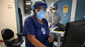 A medical professional dressed in personal protective equipment works on a computer in a medical facility.