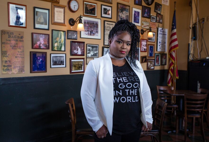 Shemekia Copeland standing in front of a wall with old photos and newspaper headlines behind her.