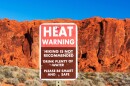 Heat warning sign informs tourists of the dangers of heat exhaustion from hiking in the desert climate. Blurred scenic red sandstone formations and desert scrub landscape background. Blue sky.