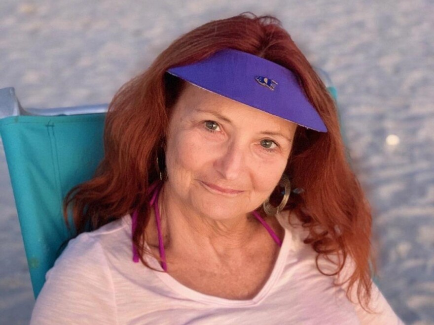 A woman wearing a purple sun visor sitting on a beach chair. 
