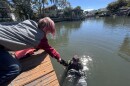 Locascio in the water of a canal while in diving gear, grabbing equipment from a child on a dock