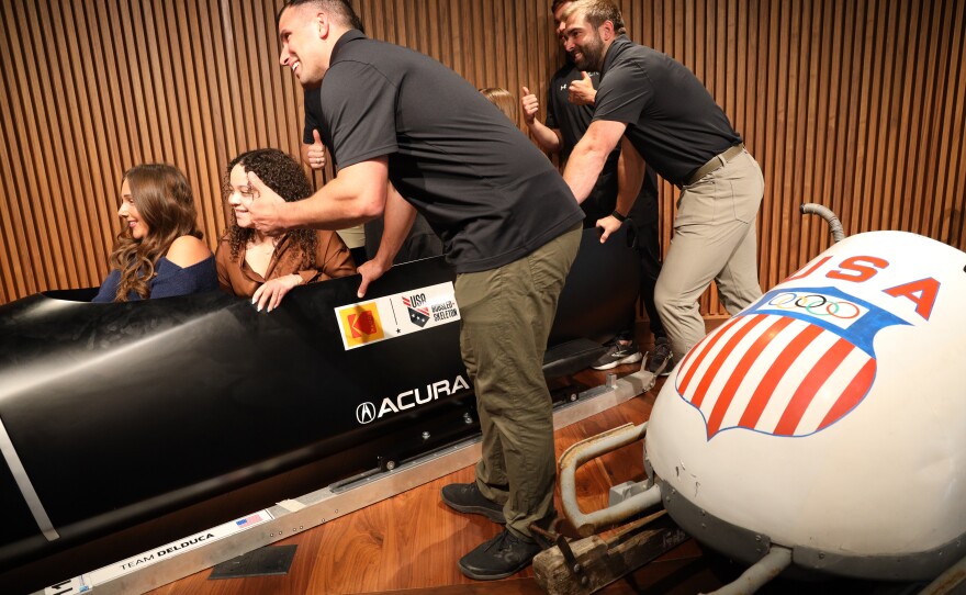 Students at the Golisano Institute for Business & Entrepreneurship pose with members of the U.S. Olympic bobsled team after Eastman Kodak Company announced its support of USA Bobsled/Skeleton ahead of the 2026 Winter Olympics, unveiling a new state-of-the-art bobsled in Kodak’s iconic yellow and red. The historic 1956 bronze medal–winning “Tyler Sled,” designed and raced by Kodak engineers, was also on display.