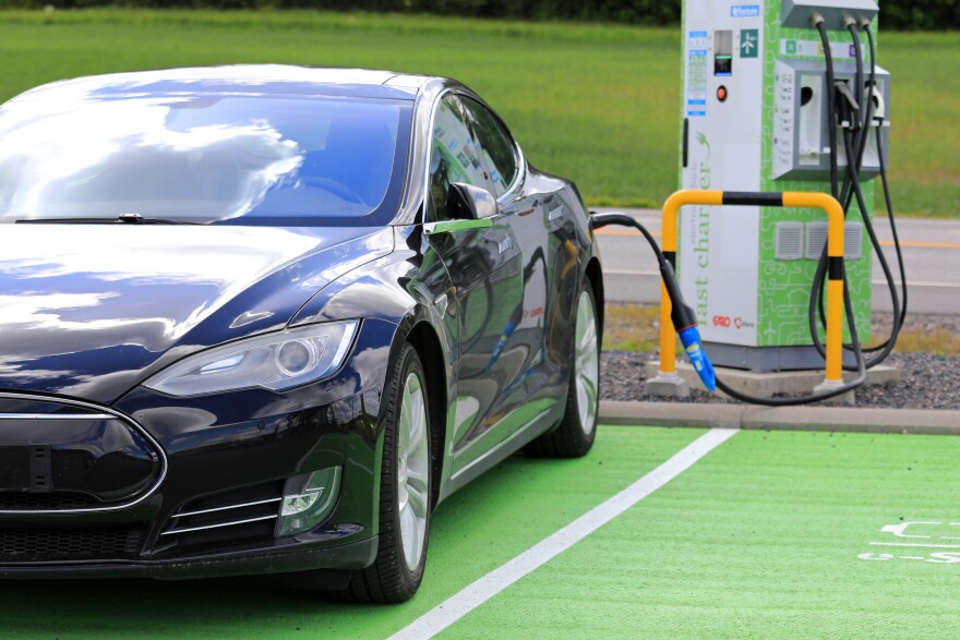 A black Tesla car in a green parking spot is hooked up to an electric charging station.