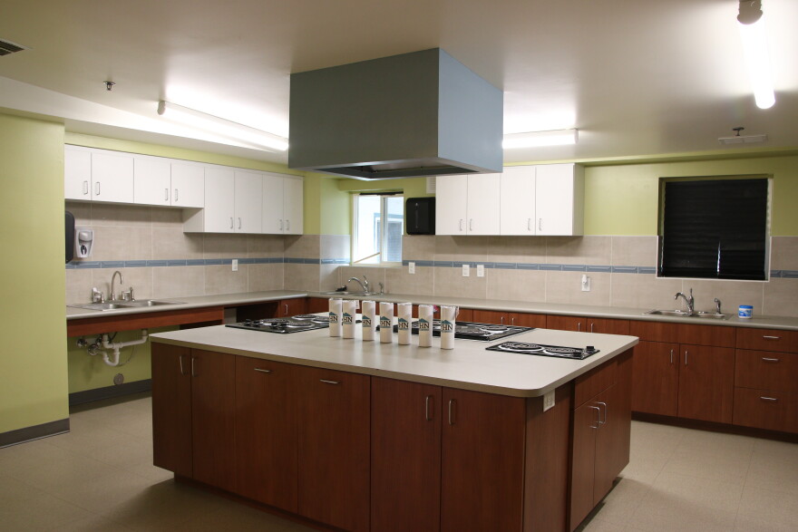 A large commercial food kitchen with wooden cabinets and a center island with several black burners.