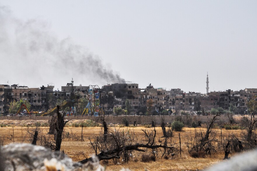 A picture taken during a Syrian army-organized tour on April 20 shows a view of Douma, on the outskirts of the capital Damascus, with a smoke plume rising in the background.