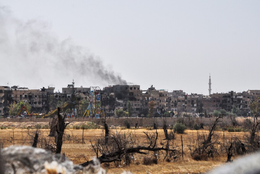 A picture taken during a Syrian army-organized tour on April 20 shows a view of Douma, on the outskirts of the capital Damascus, with a smoke plume rising in the background.