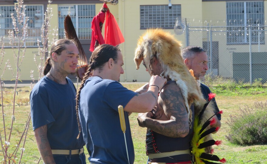 Men helping dancer with his regalia. 