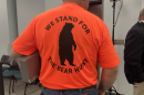 A man wearing an orange T-shirt with the slogan "We stand for the bear hunt" on the back
