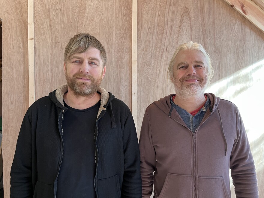 Two smiling men pose side by side for a photo. They appear to be brothers. 