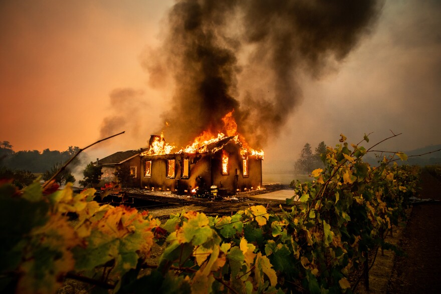 A single family home on fire, with the roof collapsed and smoke billowing into the air.