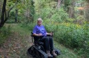A woman rides the all-terrain wheelchair on grass, with yellow flowering wildflowers beside her.