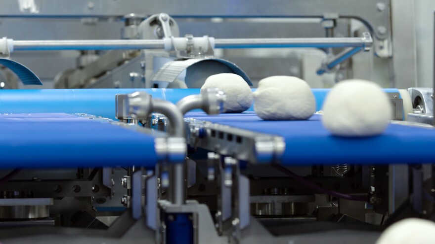 Three white dough balls sit on a bright blue conveyor belt, presumably headed toward the next step in the food prep process before being packaged and shipped off to a Domino's storefront. 