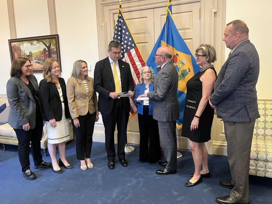 Gov. Matt Meyer swears in new indenpendent attorney general Robert Storch with their respective family members standing behind each in a row and watching them with smiles