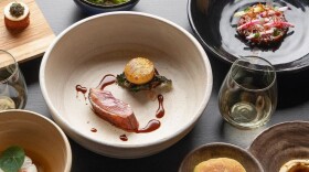 A collection of elegantly plated food arranged on a dark tabletop with beverages nearby.