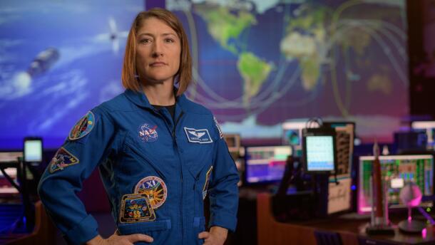 NASA astronaut Christina Koch poses for a portrait in her blue flight suit in front of the flight control room in Houston.