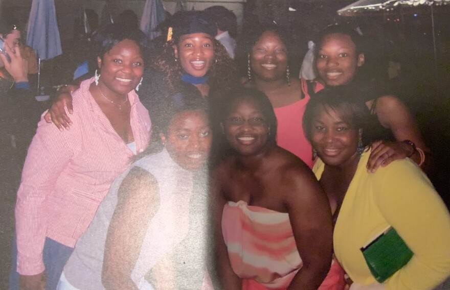 Six Black women posing around another Black woman who is dressed in a cap and gown, posing for a photo.