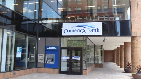 An image of the outside of Comerica Bank in downtown Ann Arbor. It is a glass building with a blue ATM next to the door. 