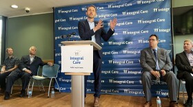A photo of Travis County Judge Andy Brown standing a podium that has a sign on it with the words "Integral Care."
