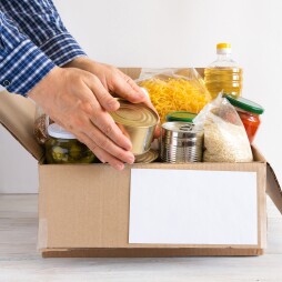 Cardboard box with butter, canned food, cereals and pasta. A donation box with various food items. The hands are placed food.