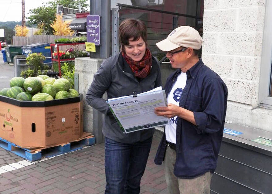 Jonathan Tong talks to Nicole Barthel about signing a petition to put Initiative 1464 on the November ballot. She signed. 