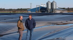 Ryan Childress (left), Dominion Energy's director of gas business development, and Kraig Westerbeek, an executive at pork producer Smithfield Foods, stand on a plastic-covered manure pond in North Carolina.