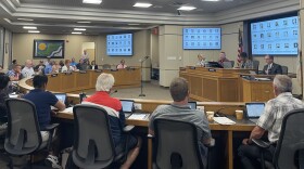 A horse shoe of county board members sit facing a large desk. 