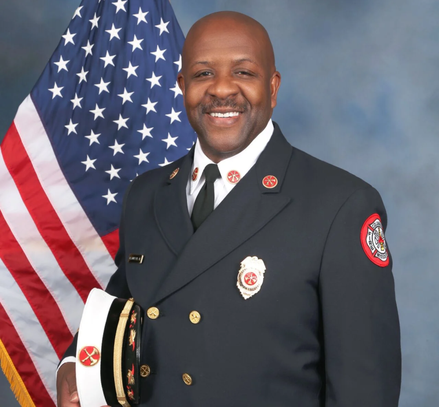 Clayton Farr poses in a suit, holding his fire chief cap on his side.