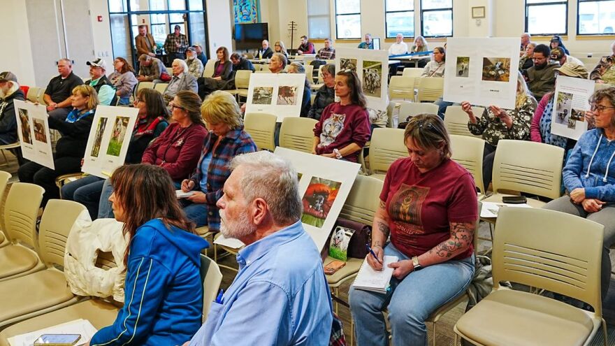 Matanuska-Susitna Borough residents hold signs during an April 21, 2026, Borough Assembly meeting displaying photos of some of the 25 dogs found dead last week at a kennel near Willow.