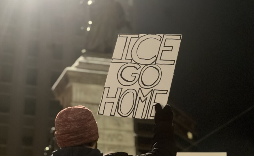 Protesters hold up signs and shout chants criticizing federal immigration enforcement activities.