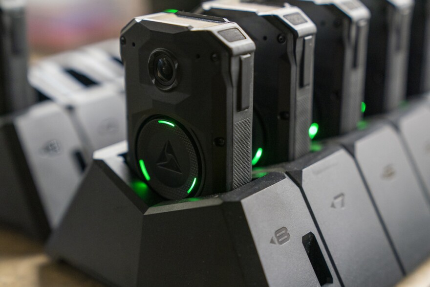 Black police body cameras lined up in charging stations.