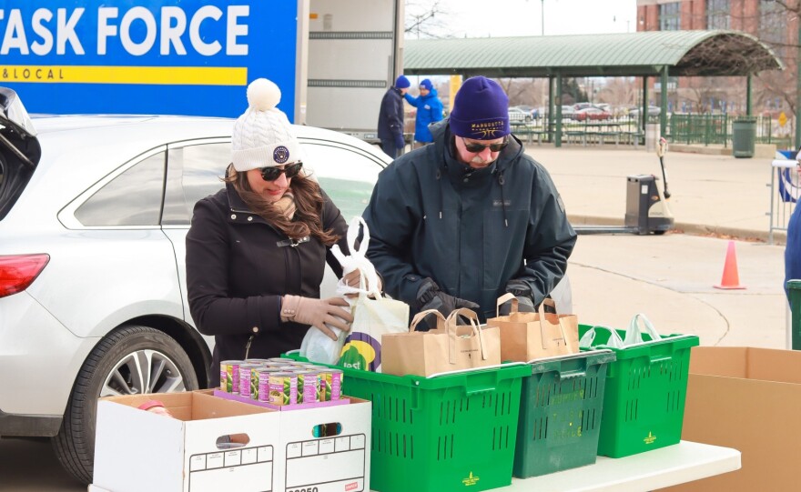 A man and a woman in cold-weather clothing sort food donation outdoors with a car in the background.