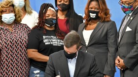 Kentucky Gov. Andy Beshear signs a bill on Friday limiting the use of no-knock warrants statewide. The governor was surrounded by members of Breonna Taylor's family including her mother, Tamika Palmer (standing behind Beshear at left). CREDIT: Timothy D. Easley/AP