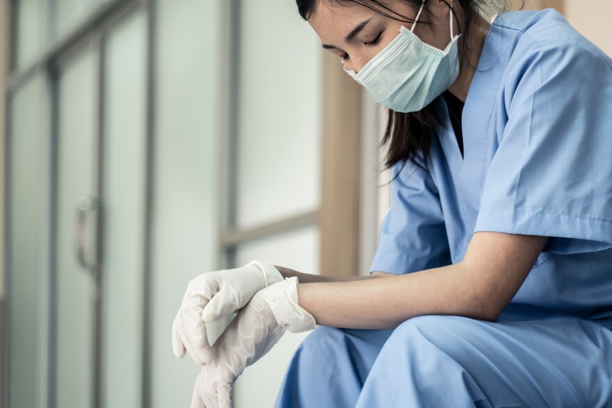 Nurse in a mask sitting, looking tired.