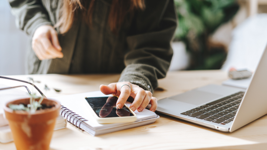 A woman working on her laptop and phone with a notebook
