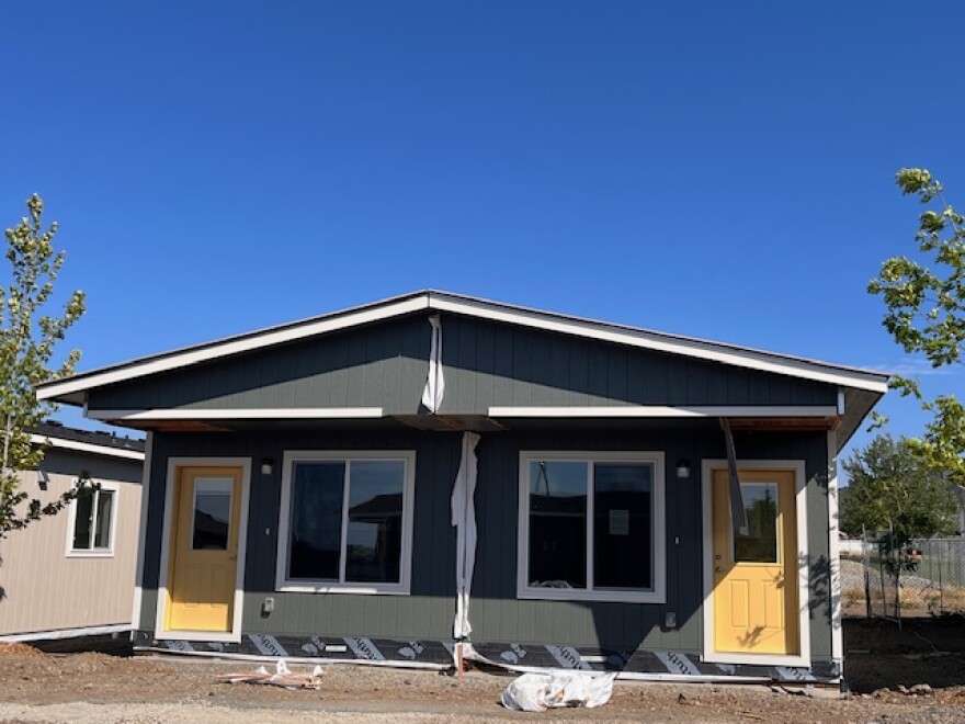 A single-story dark green duplex home with yellow doors. 