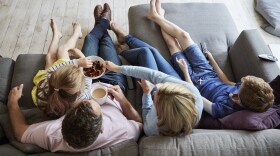 Parents and their two children seated on a sofa together. (Getty)