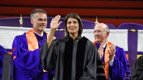FILE - In this May 10, 2018 file photo, Clemson board of trustees members, William C. Smith, left, and David H. Wilkins applaud while UN Ambassador Nikki Haley, a 1994 Clemson graduate, waves to the crowd before she gives the 2018 Commencement speech in Clemson, S.C. As she ponders her next political steps, Haley has accepted a lifetime appointment to the the Board of Trustees of Clemson University, her alma mater. The university made the announcement on Tuesday, Oct. 12, 2021. (AP Photo/Richard Shiro, File)