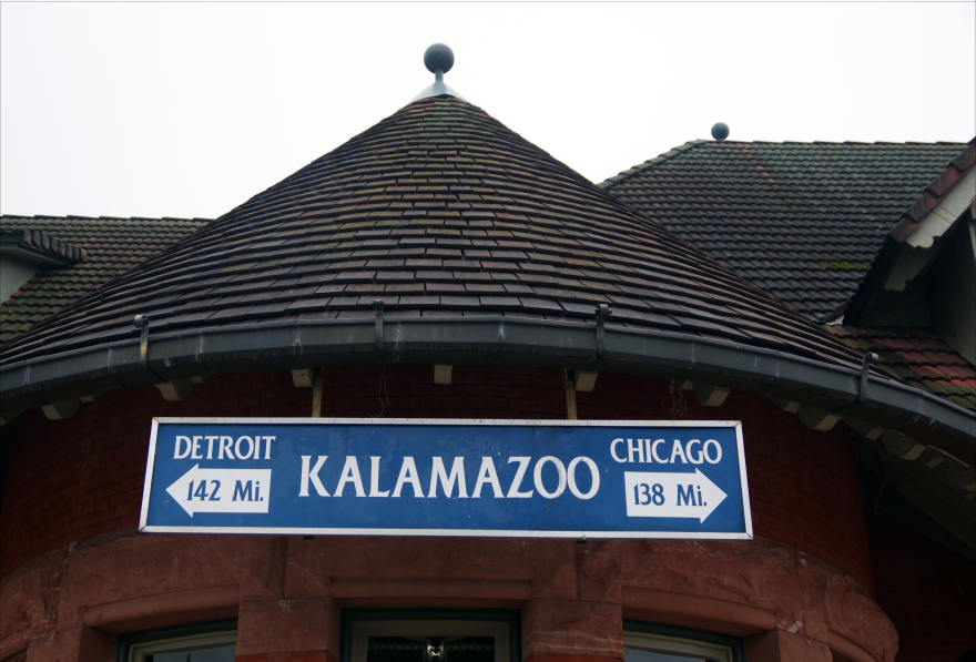 A blue sign with white lettering that says "Kalamazoo," at the train station downtown.