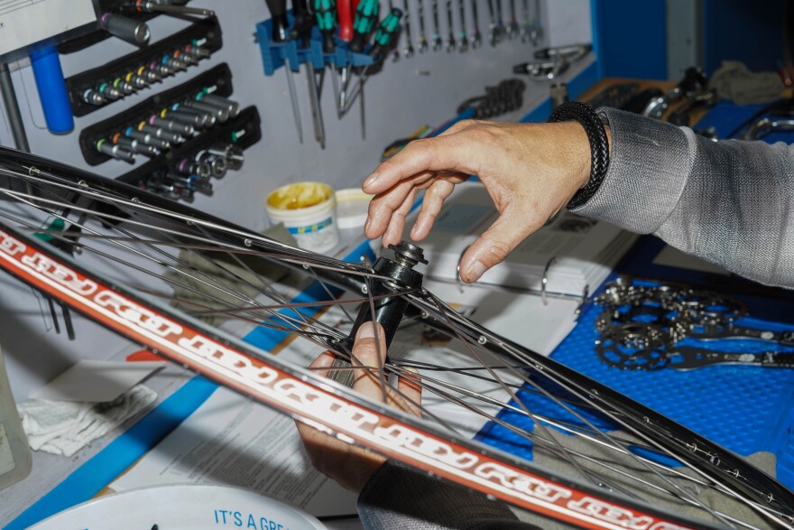 A hand reaches for a bike wheel on a work desk.