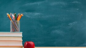 chalkboard and desk with books pencils and an apple on a desk in the foreground. 