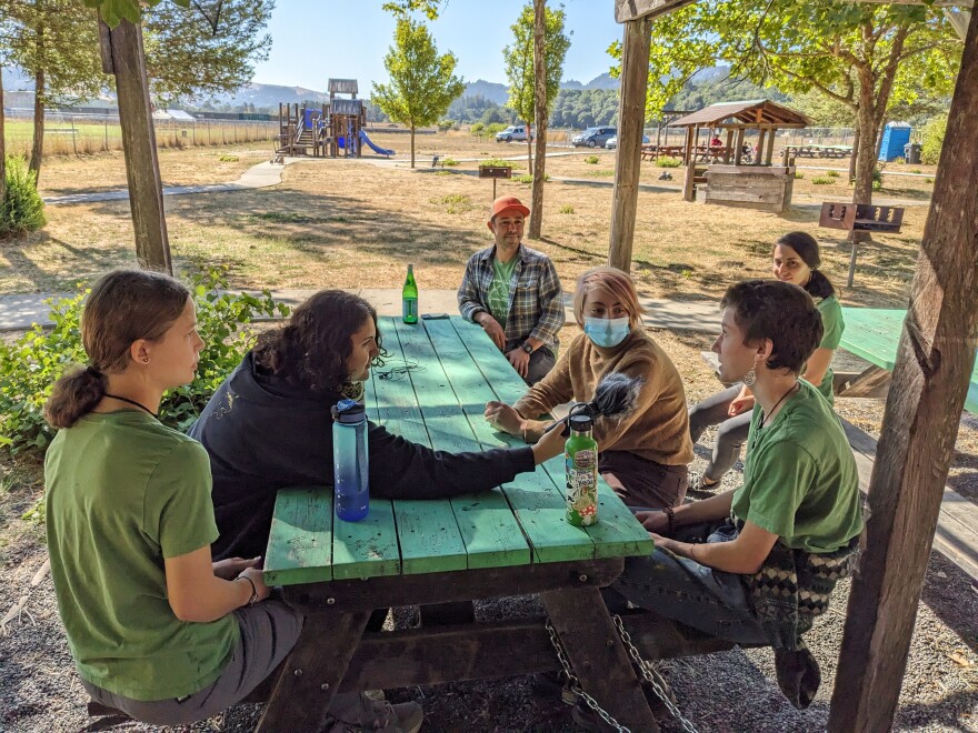 A woman leaning over a table to record an interview with young people.