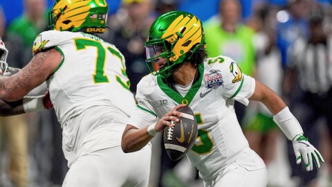 Oregon quarterback Dante Moore runs with the ball while being blocked by another Oregon player.